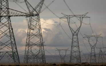 High-voltage power lines stretching across a barren landscape under a cloudy sky.