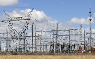 Electrical substation with power lines and pylons under a blue sky.