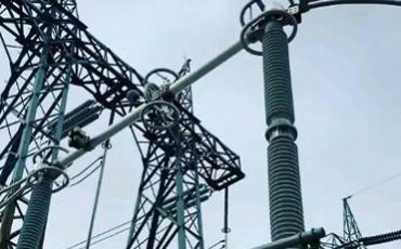 High-voltage electrical insulator and transmission tower under a cloudy sky.
