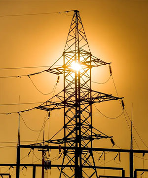 Electricity transmission tower silhouetted against a golden sunset.
