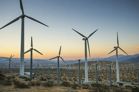 Wind turbines stand tall in a desert landscape at sunset.