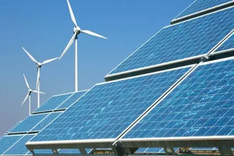 Solar panels and wind turbines under a clear blue sky producing renewable energy.